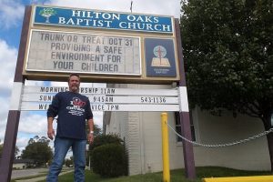 man standing outside sign for Baptist church