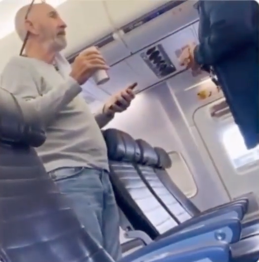 bearded man speaking with airline staff in aisle of plane 