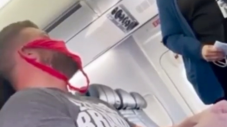 man seated in plane wearing red thong over face