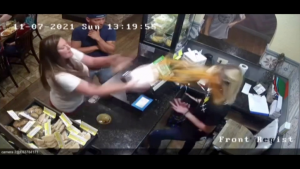 still of security camera footage showing woman throwing contents of soup container over worker's face