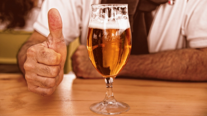 glass of beer with man with doing a thumbs up in the background